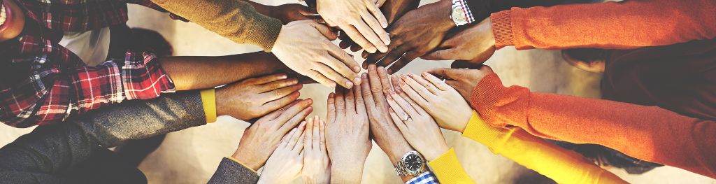 A top down view of 9 people placing both their hands on top of each other in a circle