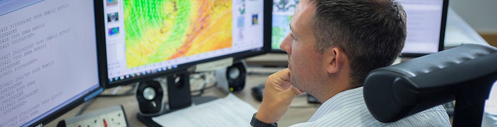 A person sitting in front of 3 computer screens examining weather charts