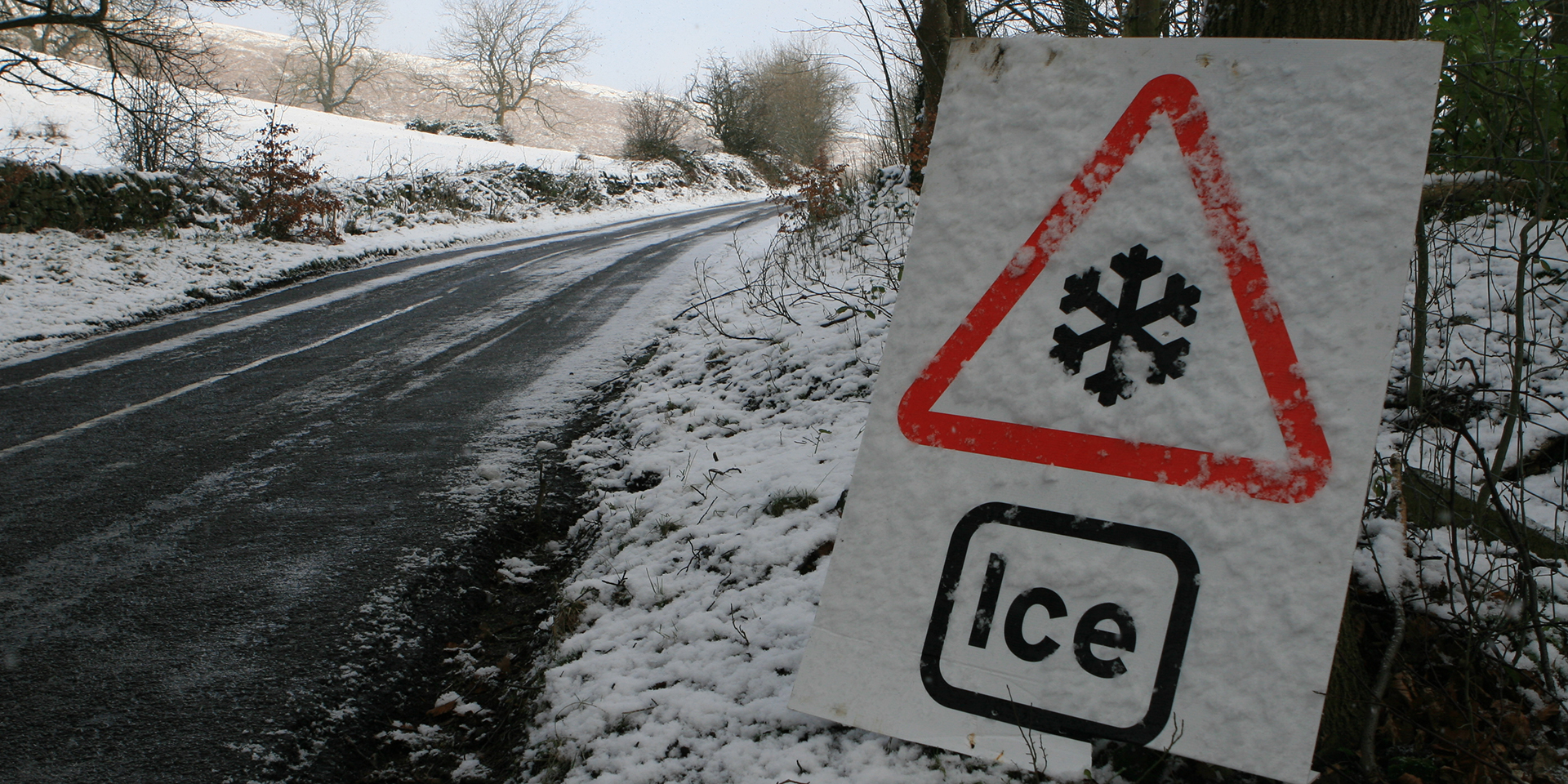 Snow and ice on a road with an ice warning sign on the side of the road.