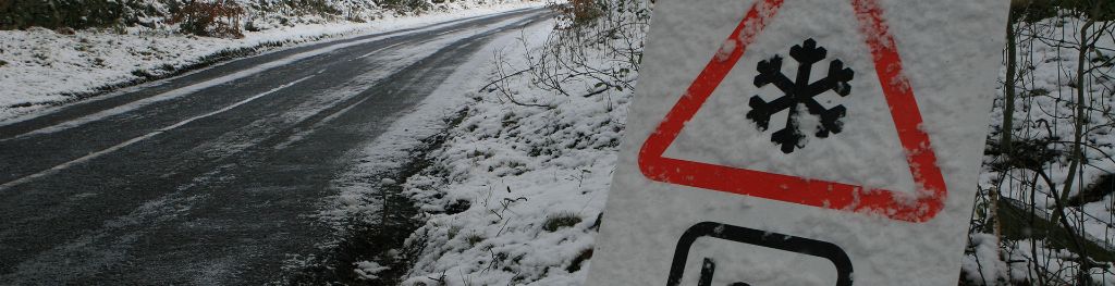 An 'ice' road sign by a snow-covered country road.