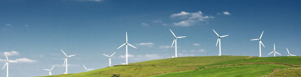 A wind farm in a green field against a blue sky with scattered clouds.