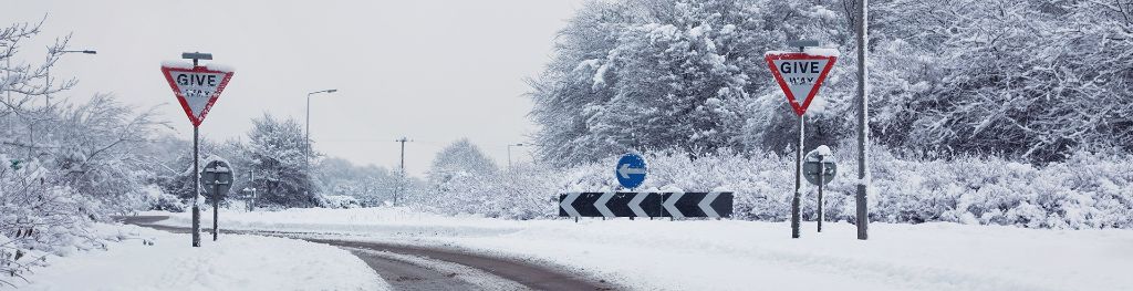 A snowy, bendy country road with traffic signs.