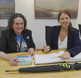 Met Office Chief Executive Penny Endersby with Minister for Natural Environment and Land Use Trudy Harrison from the Department for Environment, Food & Rural Affairs (Defra) sitting at an office table and smiling into the camera, Minister Harrison holding a pen to sign a book.