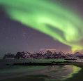 Green aurora visible above snow covered rocks by water