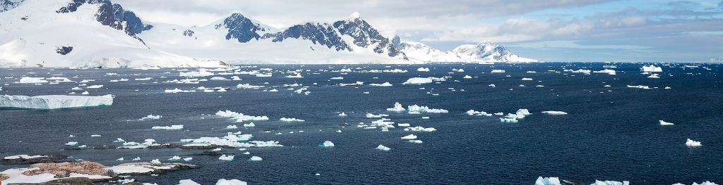 A panoramic view of the Antarctic coastline and sea with sea ice on the surface.