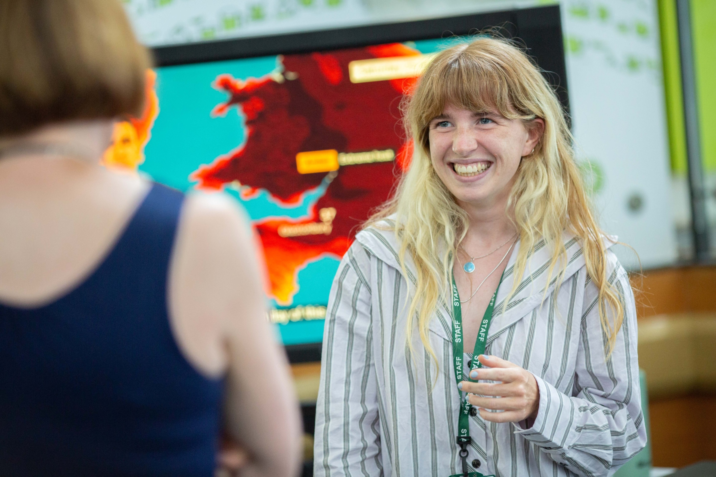 This image shows a person smiling at someone else who is partially in view. There is a weather map in the background.