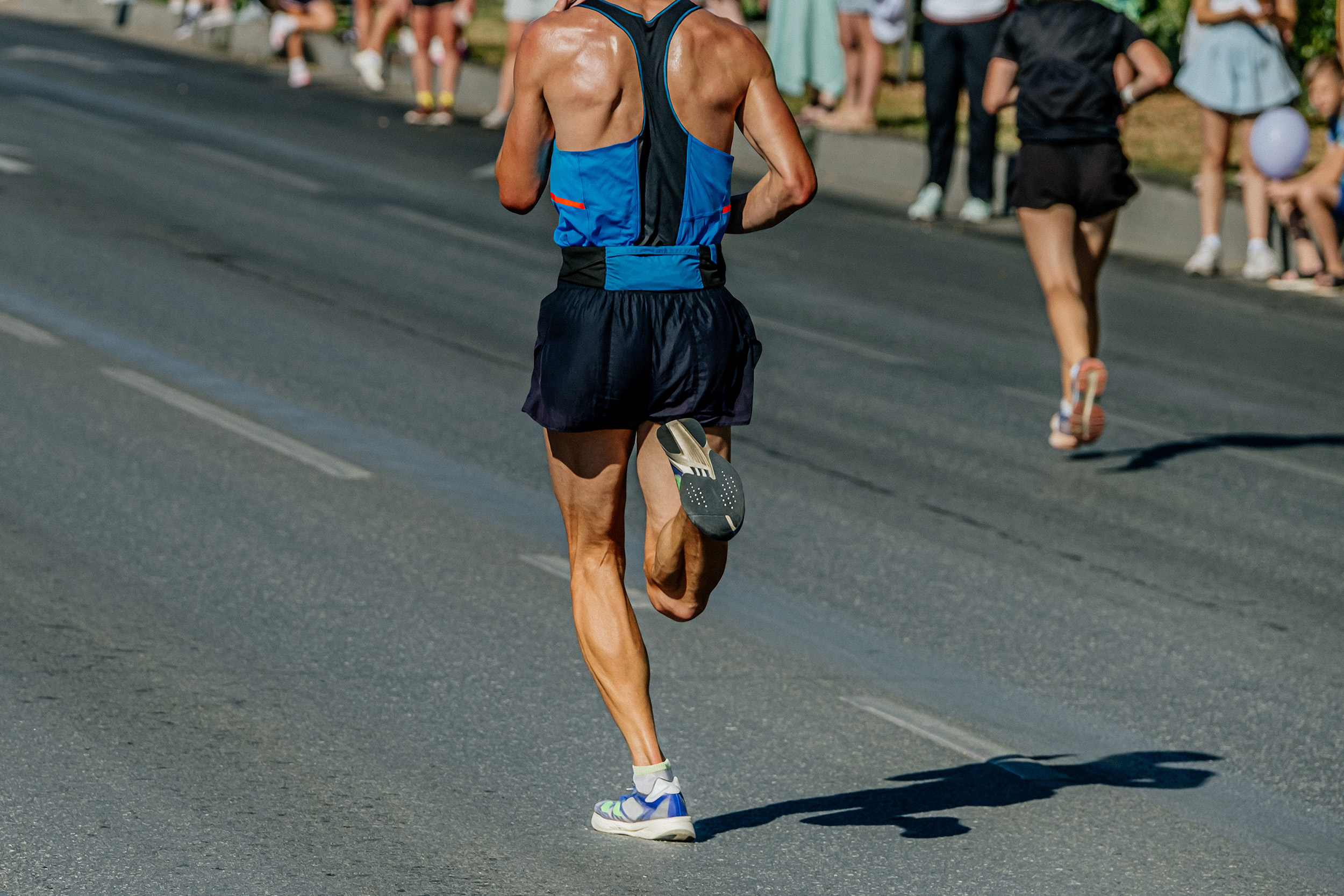 Man running on a road in blue trainers, black shorts and a blue and black vest. Very toned man.