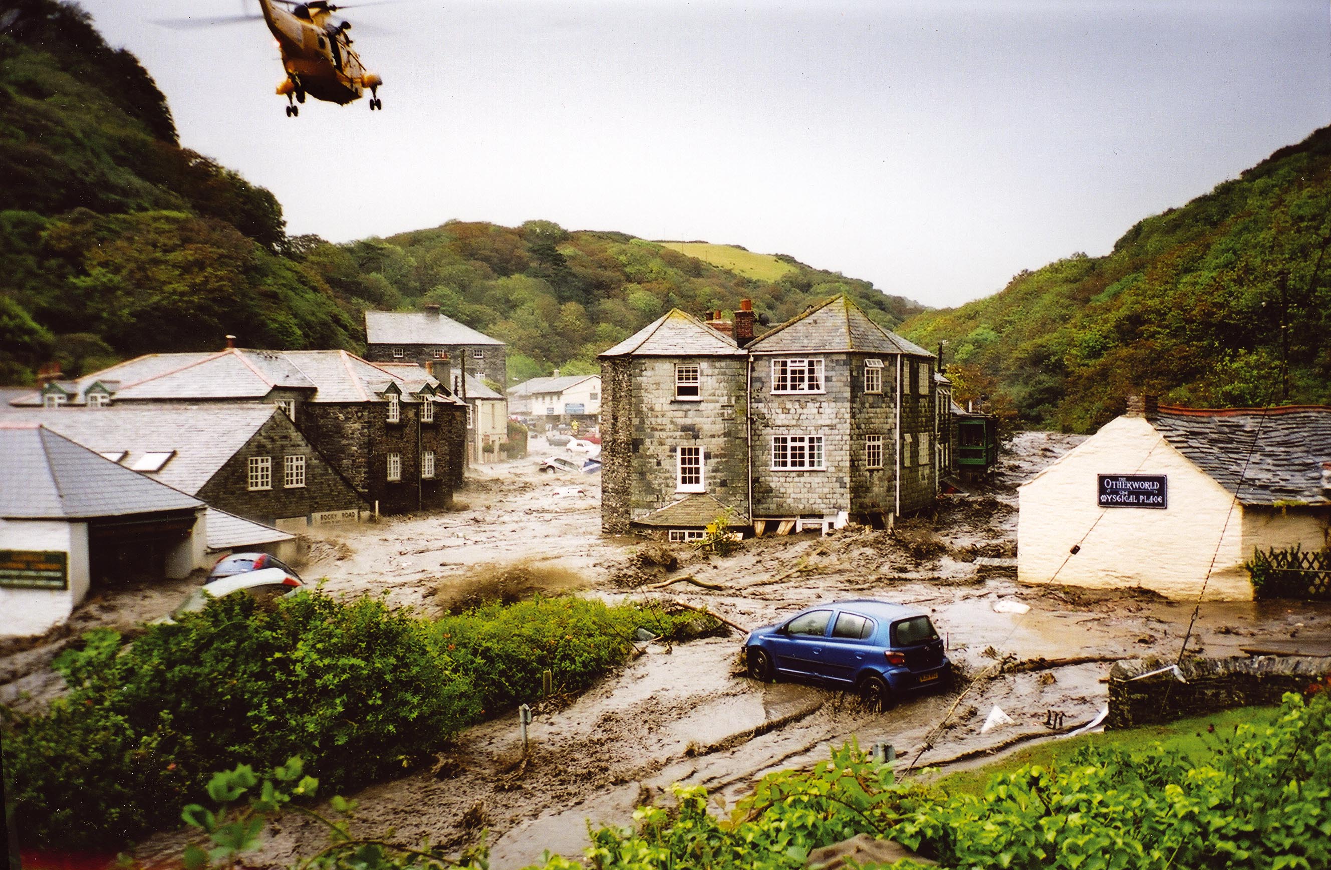 Helicopter in the air over a flooded Boscastle. Flood water is rushing down through the village with cars and debris everywhere.