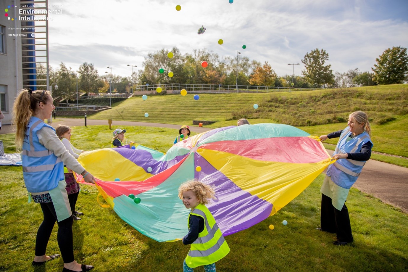 Children playing on a grass field with colourful balls and parachute.